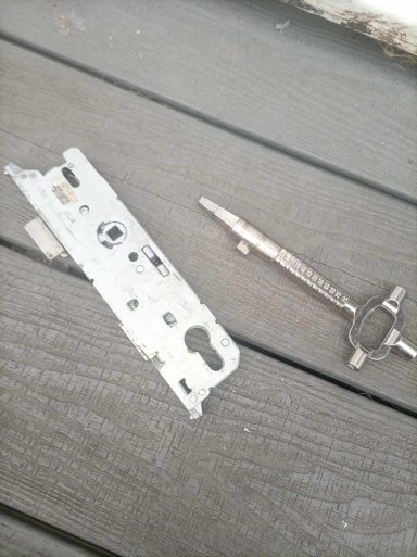 A metallic door lock mechanism beside a silver compass tool on wooden surface.