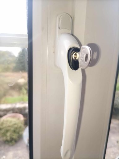 Close-up of a white window handle with a keyhole, mounted on a window frame.